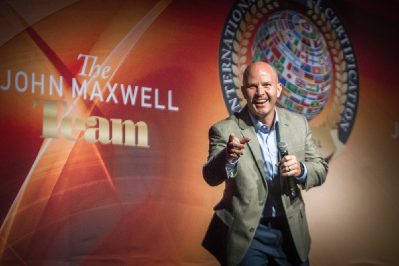 Kent Hyer on stage as a John Maxwell Team certified trainer, pointing toward the audience